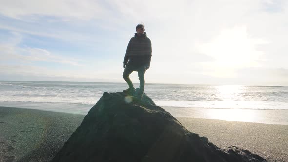 Man Traveler Standing on a Huge Stone on Volcanic Black Sand Beach in Iceland