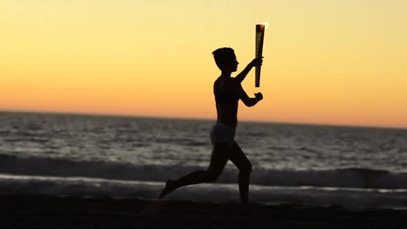 Woman running with a simulated Olympics torch on the beach at sunset.