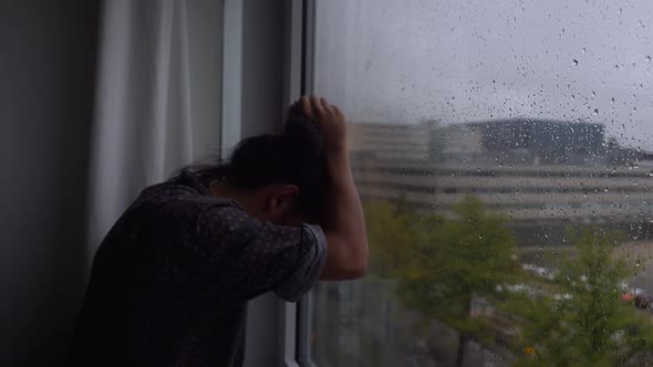 A young man in total desperation in front of a rainy window, all is lost, there's no hope left in hi