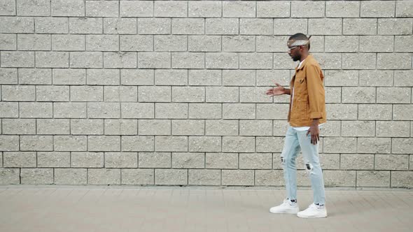 Side View of Funny African American Man Performing Robot Dance Outdoors Against Brick Wall