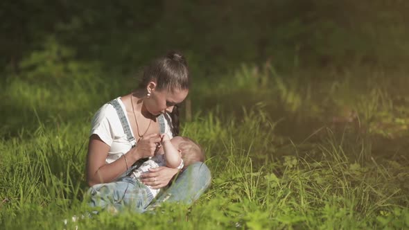 Young and Happy Mother Feeding Her Baby in the Summer on the Nature Outdoors. Breastfeeding and
