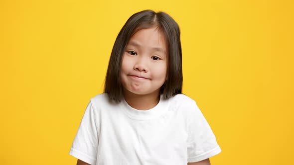 Clueless Asian Little Girl Shrugging Shoulders Posing Over Yellow Background