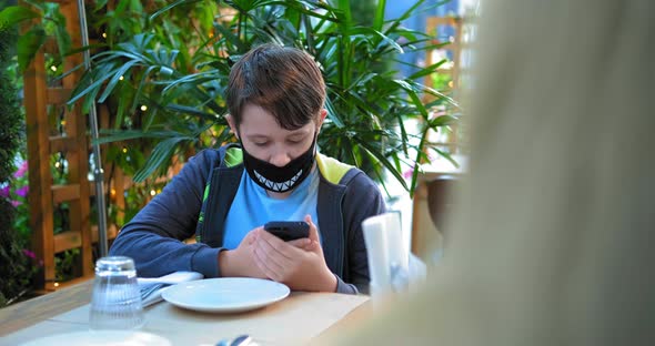 Young Guy in Black Designed Face Mask Types on Smartphone