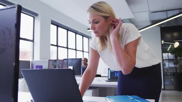 Caucasian businesswoman standing using laptop in office with coworker in background