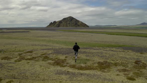 Aerial drone view following a person running on a green field, towards a mountain, in Iceland