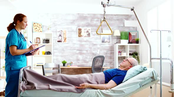 Nurse Checking on Old and Sick Patient Lying in Hospital Bed