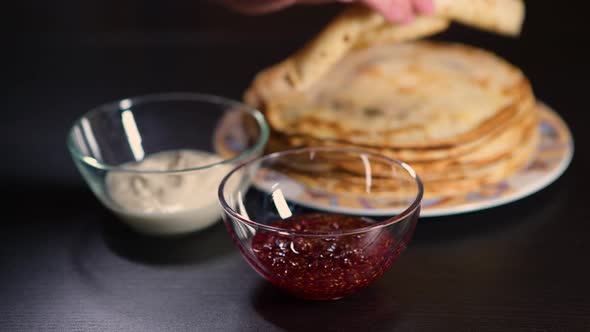 girl takes a twisted pancake and dips it in jam