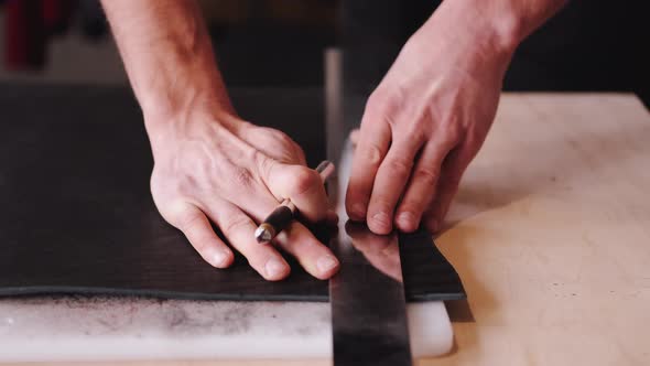 The Tanner Is Cutting Black Leather Sheet with a Razor and Metre