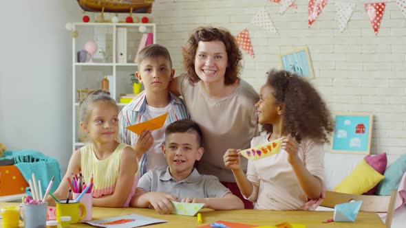 Happy Female Teacher and Multiethnic Children Posing with Origami Boats