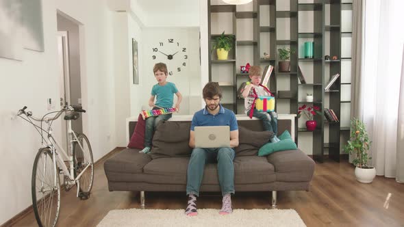 Young Father Looks After The Children At Home And Works At The Computer.