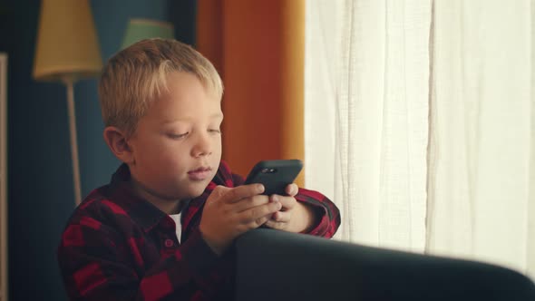 Young Boy Sitting on the Couch and Playing Games on the Smart Phone