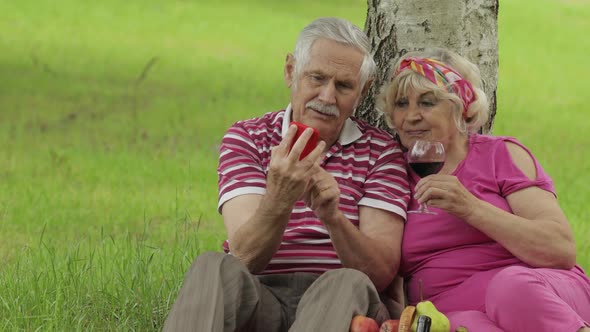 Family Picnic. Senior Old Grandparents Couple in Park Using Smartphone Online Browsing, Shopping