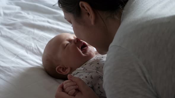 Loving Mother Talks and Kisses Cheeks of Little Daughter Holding Hands