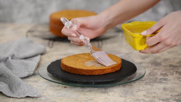 Unrecognizable female confectioner hand soaks sponge cake with sweet caramel syrup.