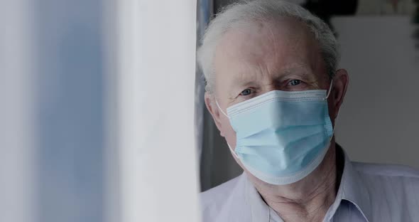Portrait of Sad Grandfather in Medical Mask Looks at Camera Anxiously at Home