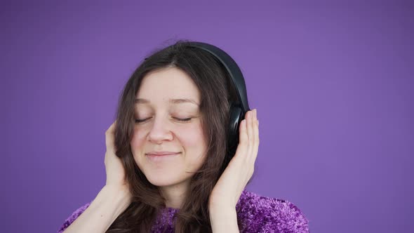 Cute Darkhaired Woman Listens to Music with Headphones on a Purple Background