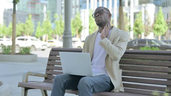 African Man with Neck Pain Using Laptop While Sitting Outdoor on Bench