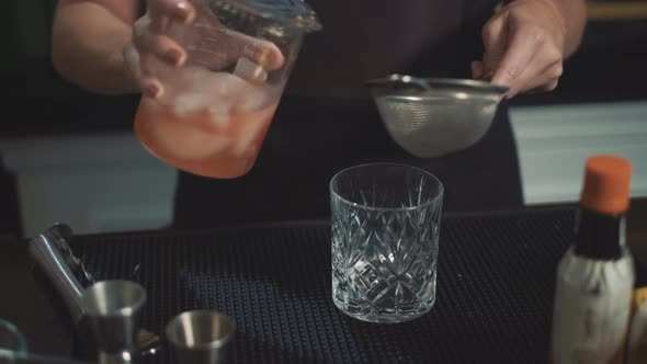 mixologist strains mixed drink into glass, preparing craft cocktail.