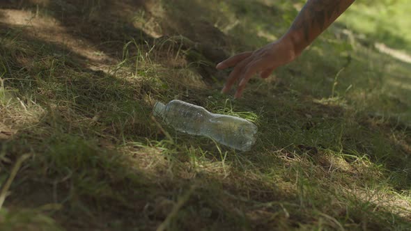 Closeup of Black Female Hand Picking Up Used Plastic Bottle From Green Grass