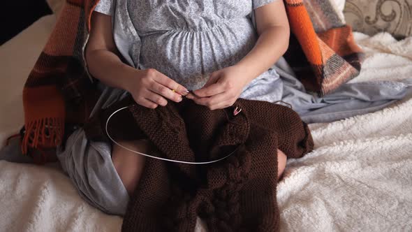 A Pregnant Woman Knitting for Her Baby a Warm Clothes Sitting on Bed Closeup