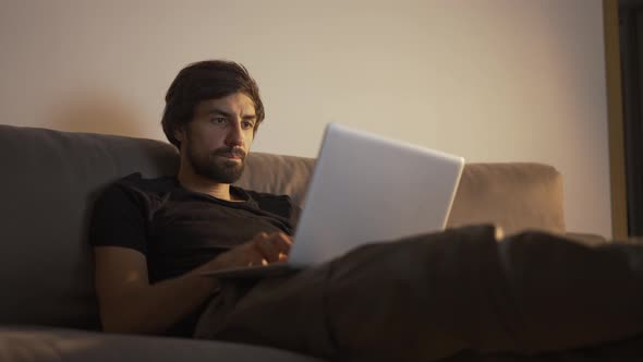 Concentrated Man Working on a Laptop at Home While Sitting on the Couch