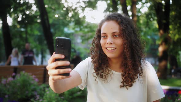 Portrait of smiling teenage girl having video call by mobile phone outdoors. Beautiful person.