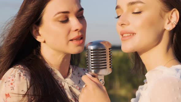 Two Attractive Women in White Dresses Sing Into Retro Shiny Microphone