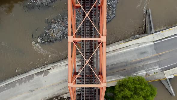 Railroad is running through a steal bridge and above regular asphalt road and river. Areal top view.
