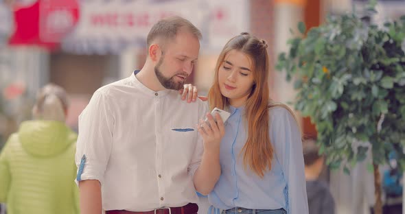 Couple in the Mall Looks at the Phone and Discuss Something