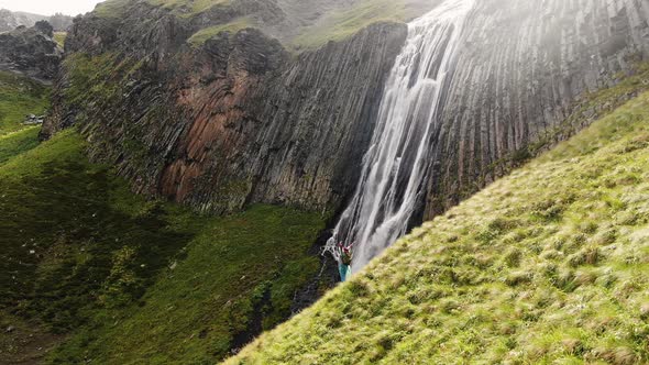 Lady Stands on Green Hillside Near Mountainous Waterfall