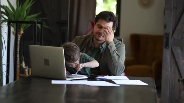 Father is trying to work and play with a little boy at same time at home.