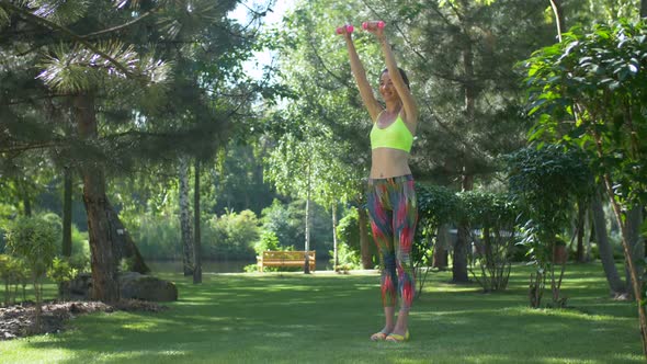 Active Woman Exercising Using Dumbbells in Park