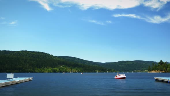 Timelapse of lake surrounded by green trees and mountains with floating boats and ships