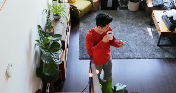 Man with coffee cup using mobile phone in living room 4k