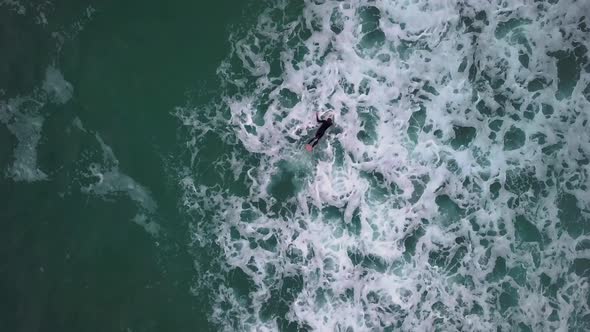 Birds-eye-view of surfer duck-diving choppy waves. Drone-shot.