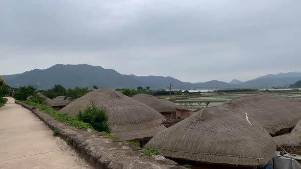 Pov walk on path showing traditional houses in korean village during cloudy and mountains in backgro