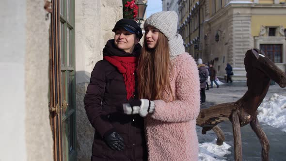 Two Smiling Women Tourists Looking at Shop Window on City Street Family Couple Talking Embracing