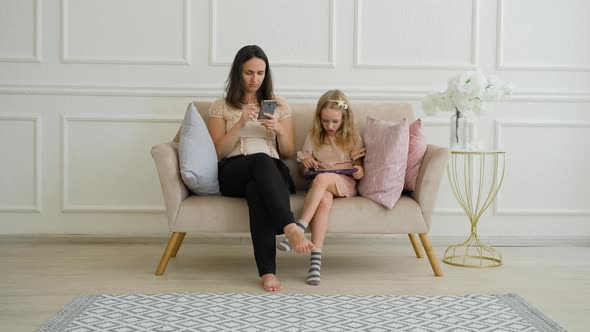 Young Woman with Daughter Using Gadgets on Sofa