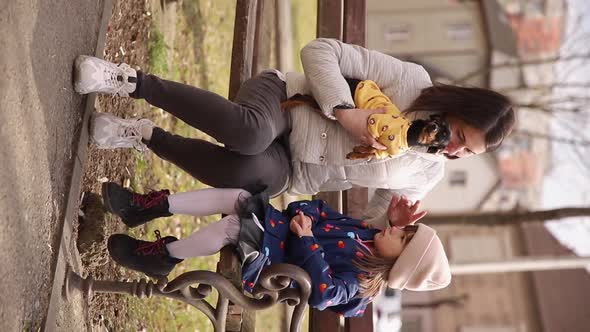 Vertical Video of Mom Sits with Daughter and Little Dog on the Bench