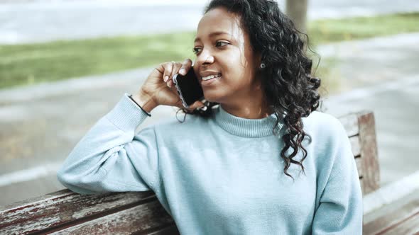 Pleased brunette African woman wearing blue sweater talking by mobile