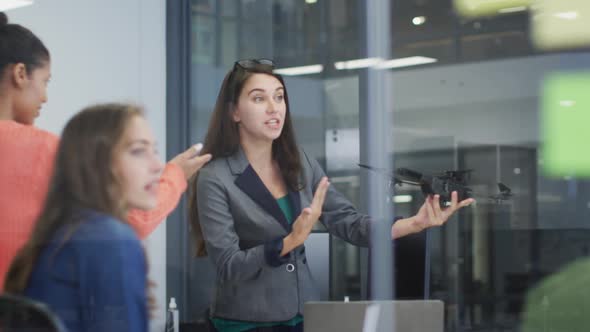 Caucasian woman holding drone giving presentation to diverse group of colleagues