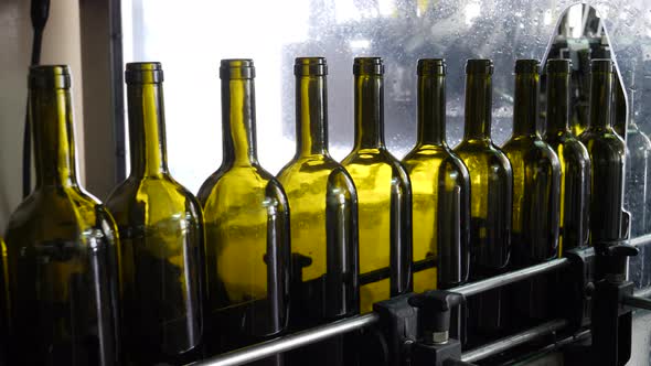 A row of glass wine bottles moves down a production conveyor belt in a factory