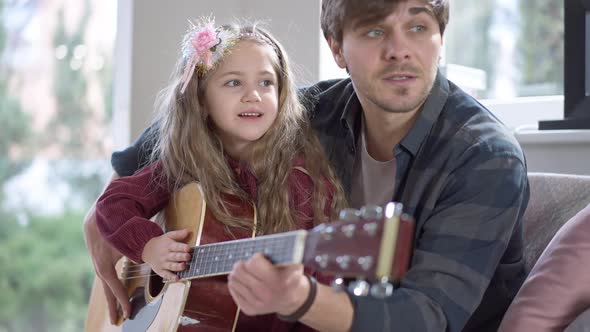 Portrait of Charming Beautiful Caucasian Little Girl Playing Guitar with Blurred Man Talking