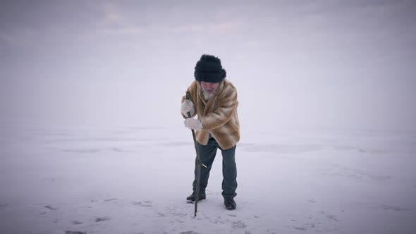 Wide Shot Bearded Senior Man Hitting Stick on Ice in Slow Motion Standing on Frozen Ocean