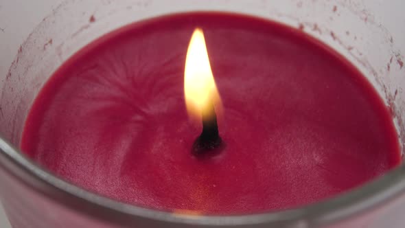 Flame of a red candle flickers in a glass container close-up