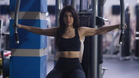 Portrait of Confident Concentrated Middle Eastern Woman Exercising in Seated Chest Fly Machine