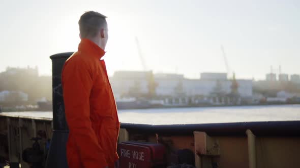 Harbor Worker in Orange Uniform Standing By the Board of the Ship and Resting