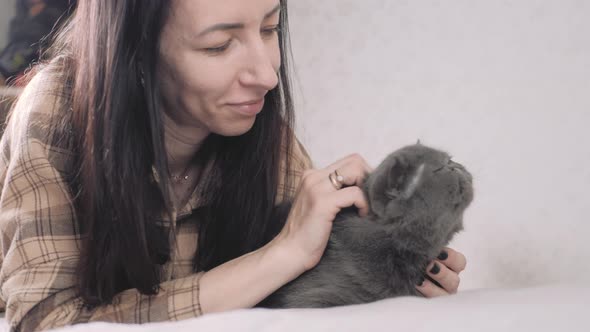 A Young Woman is Stroking a Gray Cat Lying on the Bed