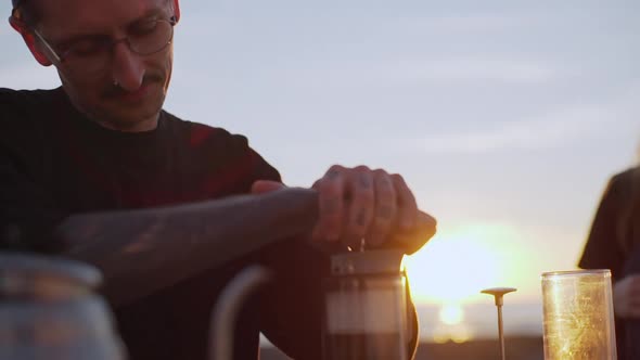 Extraordinary Tattooed Man Making Coffee By Special Method on Nature with Female Companion at Dawn