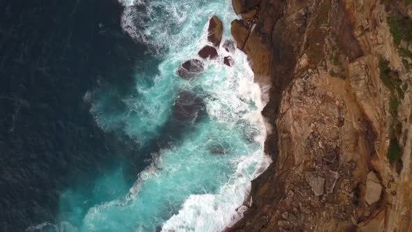 Ocean waves crashing and hitting against cliff and rocks bird eye view aerial drone shot.